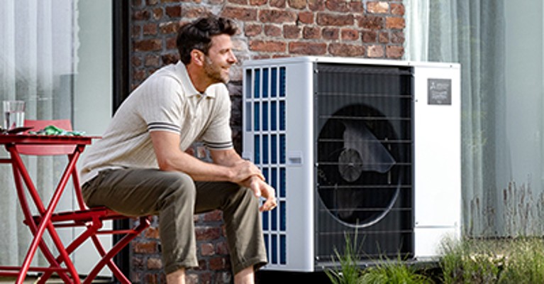 Person sitzt auf einer Terrasse neben einer installierten Mitsubishi Electric Wärmepumpen-Außeneinheit
