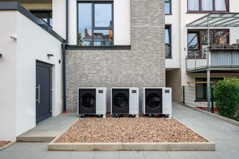 Photo of three cascaded air/water heat pumps in front of an apartment building