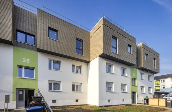 Mehrgeschossiges Wohngebäude mit moderner Dachaufstockung und Holzfassade unter blauem Himmel