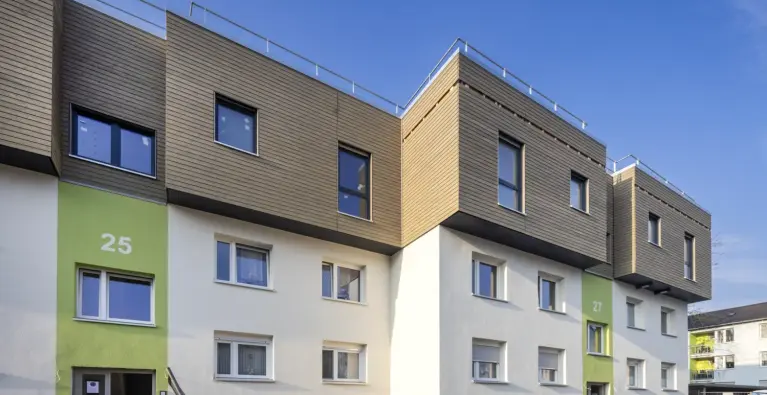 Mehrgeschossiges Wohngebäude mit moderner Dachaufstockung und Holzfassade unter blauem Himmel