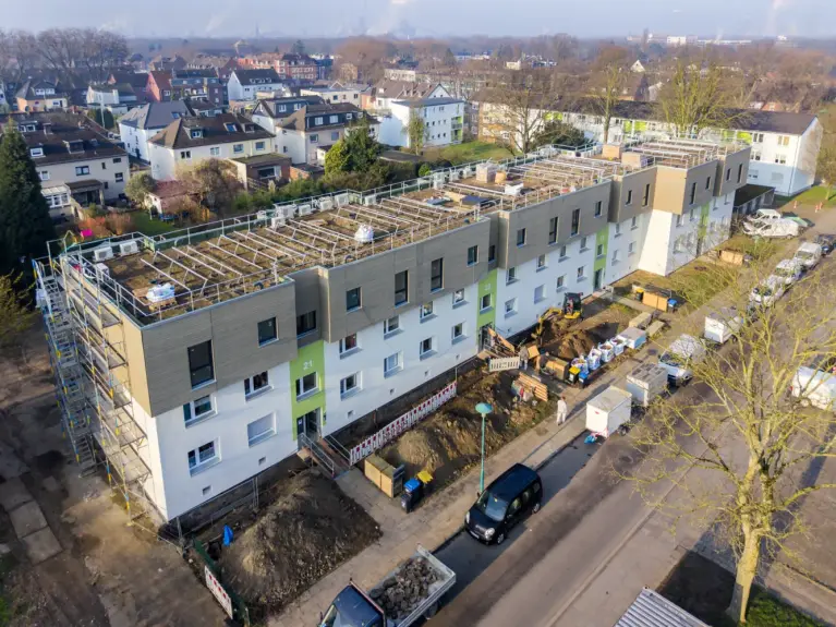 Sanierter Wohnblock mit aufgestocktem Dachgeschoss und umliegender Stadtbebauung aus der Vogelperspektive