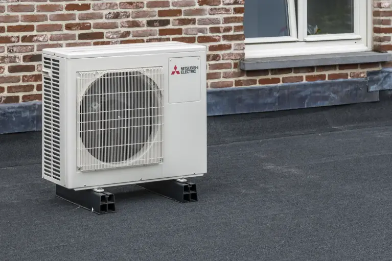 Außengerät einer Wärmepumpe von Mitsubishi Electric, installiert auf Flachdach vor Backsteinfassade.
