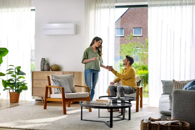 Modernes Wohnzimmer mit Klimaanlage an der Wand, hellen Fensterfronten und gemütlichem Sitzbereich. Zwei Personen verbringen Zeit im Wohnraum.