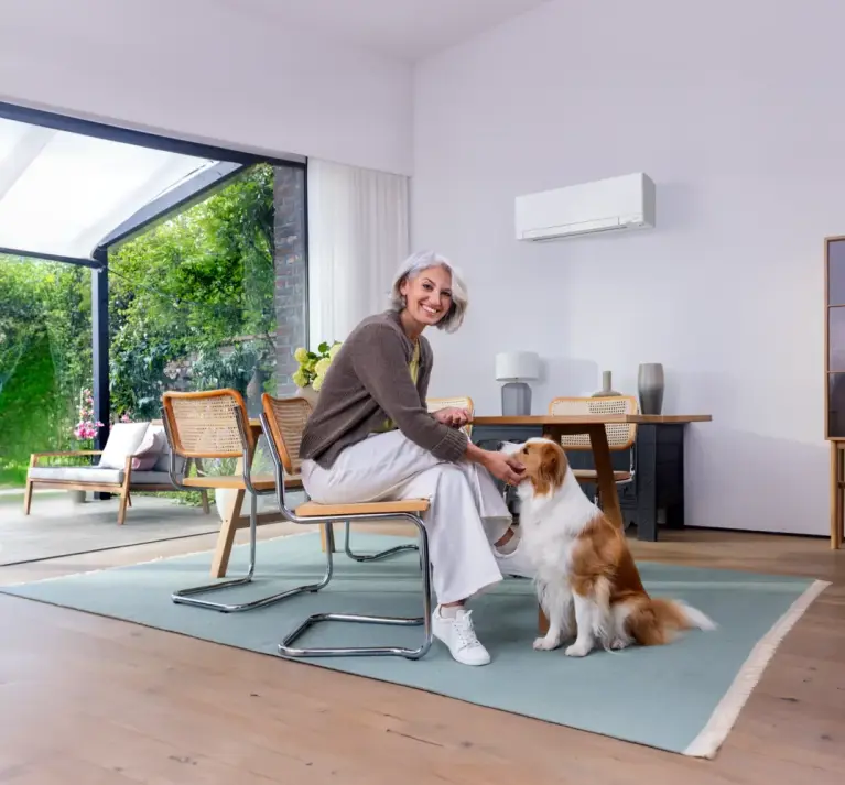 Abbildung eines Esszimmers mit weißem MSZ-LN Wandgerät und Frau mit Hund im Vordergrund Abbildung eines Esszimmers mit weißem MSZ-LN Wandgerät und Frau mit Hund im Vordergrund