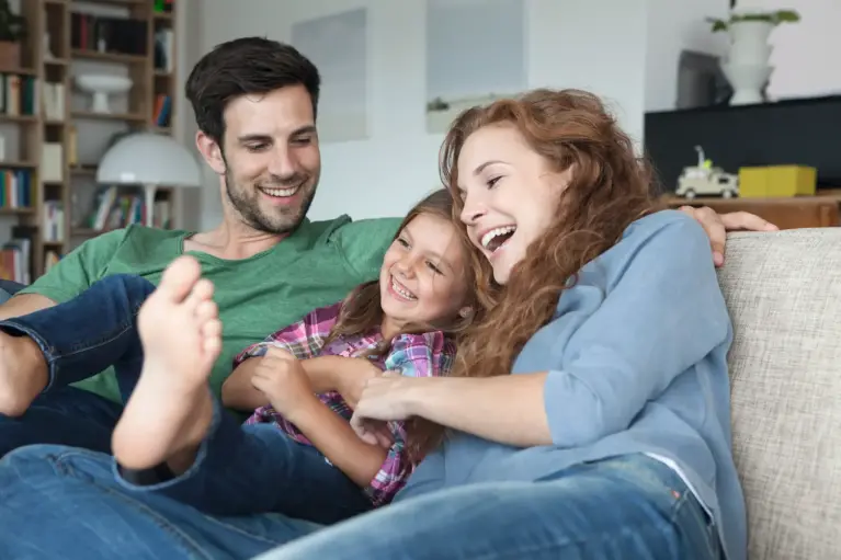 Famille assise sur le canapé - le père à gauche, leur fille au milieu et la mère à droite