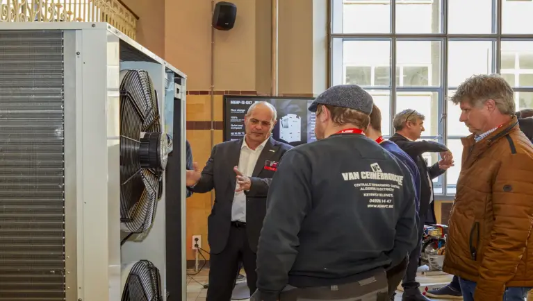 Medewerker Mitsubishi Electric geeft uitleg aan drie bezoekers over werking van een buitenunit 