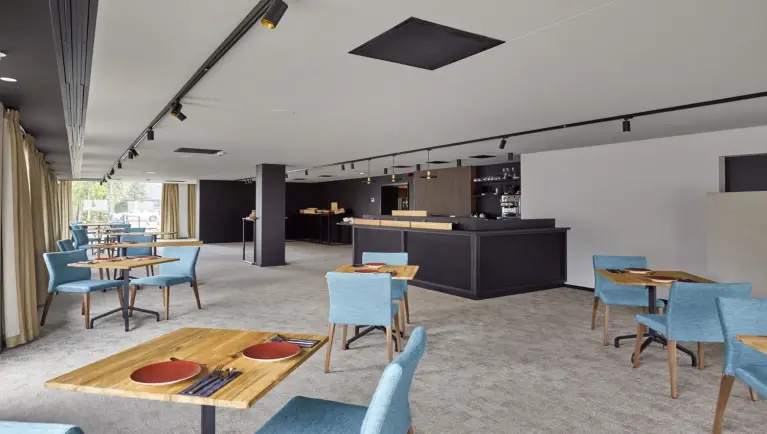 Eetruimte met houten tafels en lichtblauwe stoelen, in het midden staat er en zwarte bar
