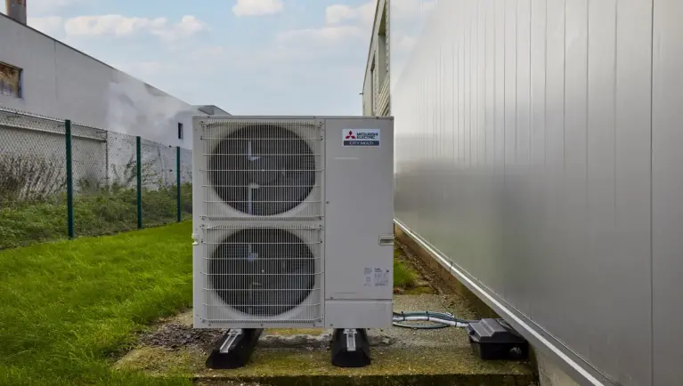 Witte buitenunit staat naast gebouw met daarrond gras