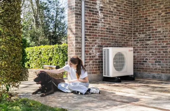 Une fille caresse son chien sur une terrasse devant une pompe à chaleur