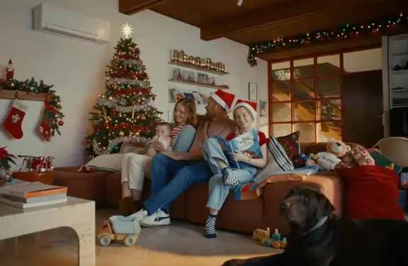 La famille est assise ensemble dans le canapé, avec le sapin de Noël en arrière-plan.