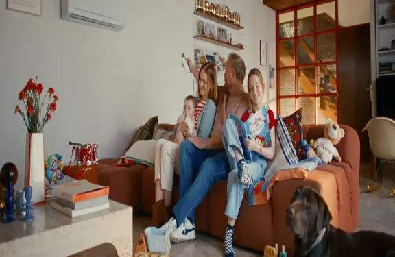 La famille est assise sur le canapé du salon et le père met en marche le climatiseur à l'aide de la télécommande. La famille est assise sur le canapé du salon et le père met en marche le climatiseur à l'aide de la télécommande.