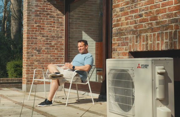 Un homme profite du soleil sur sa terrasse, avec la pompe à chaleur à côté de lui.